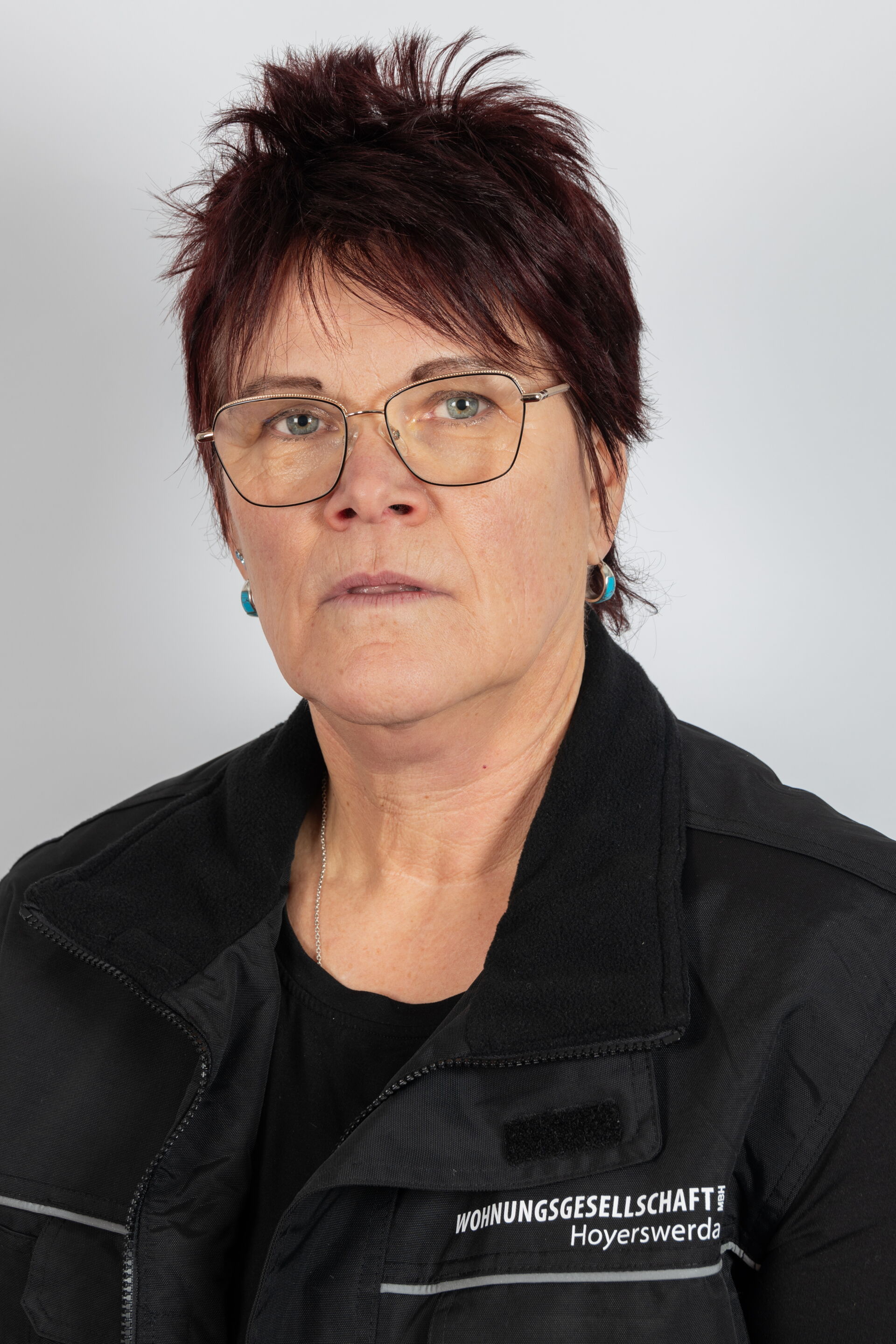 Portraitfoto - Frau mittleren Alters mit Brille & dunklem Kurzhaarschnitt in schwarzem T-Shirt mit Firmenlogo