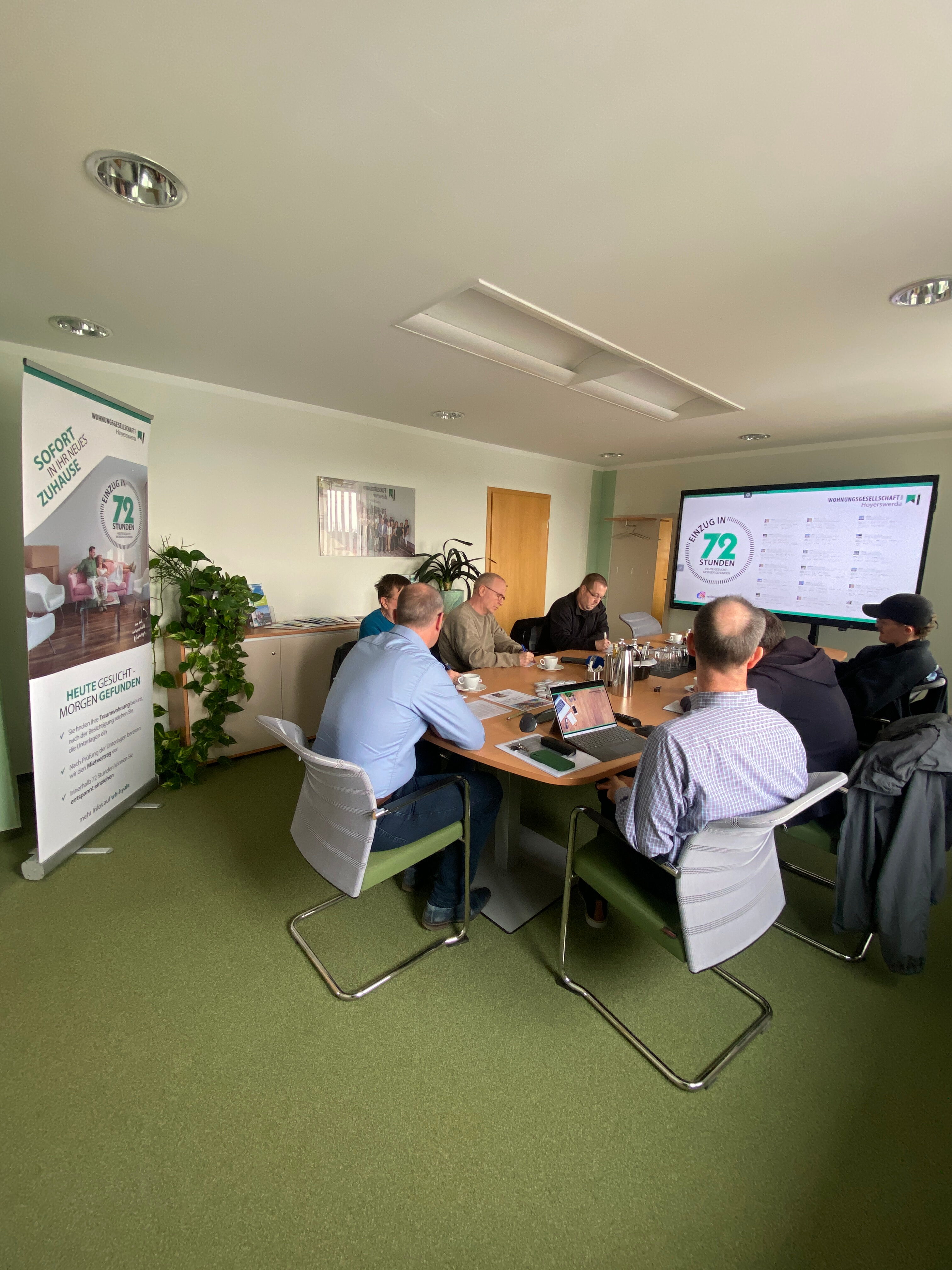 Team der Wohnungsgesellschaft mbH Hoyerswerda bei Besprechung zum 72-Stunden-Einzug vor Monitor und Banner.