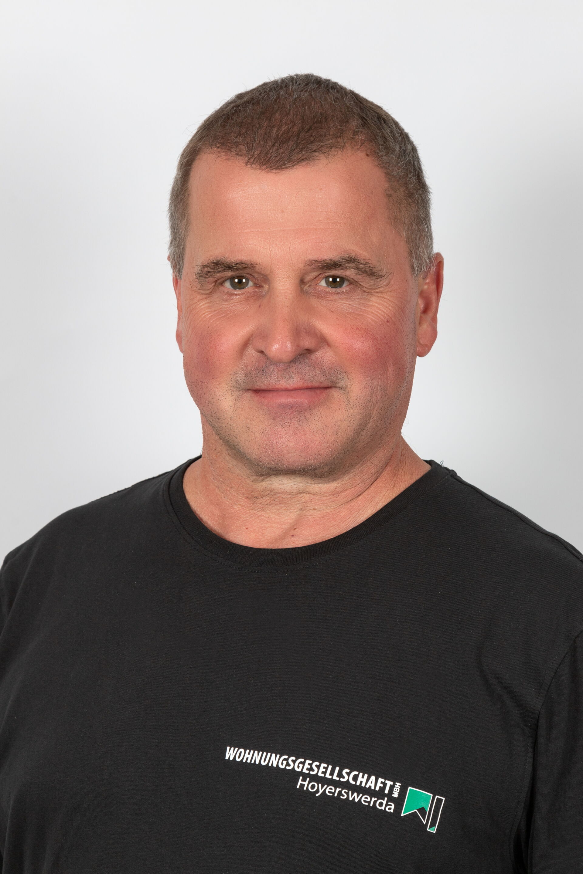 Portraitfoto - Mann mittleren Alters mit graumeliertem Haar & schwarzem T-Shirt mit Firmenlogo