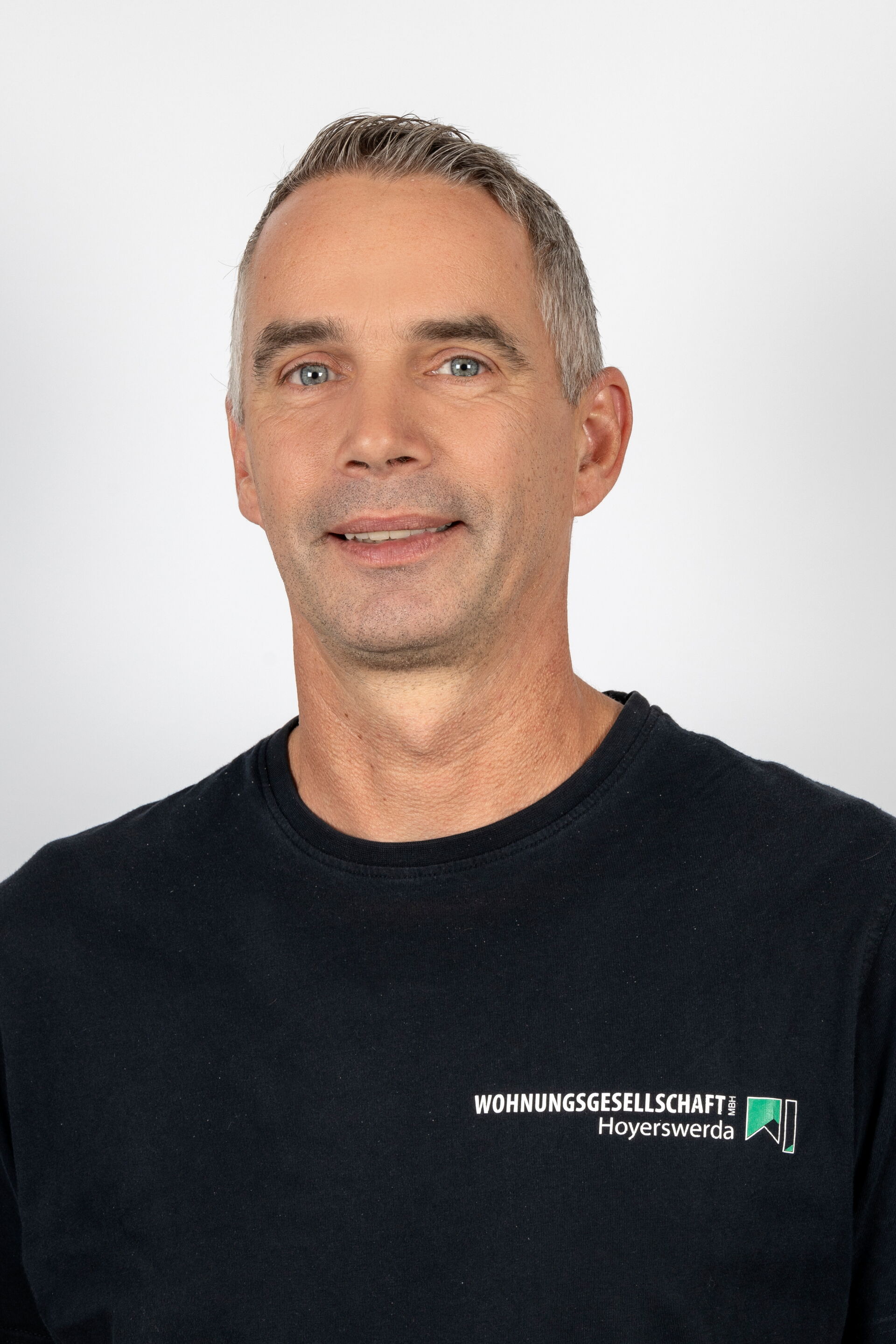 Portraitfoto - Mann mittleren Alters mit graumeliertem Haar & schwarzem T-Shirt mit Firmenlogo
